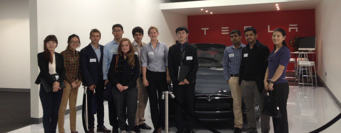 a group of students posing in front of a Tesla car