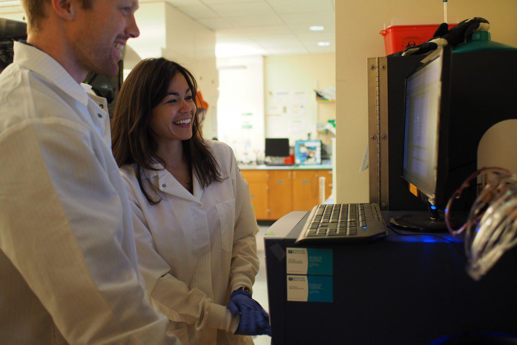 two people in lab coats smiling at a computer