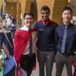 students wearing capes next to a project display