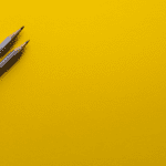 Two silver pencils on a yellow background.
