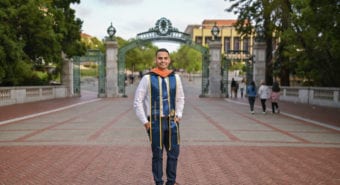Hector Gomez in front of Sather Gate with graduation regalia