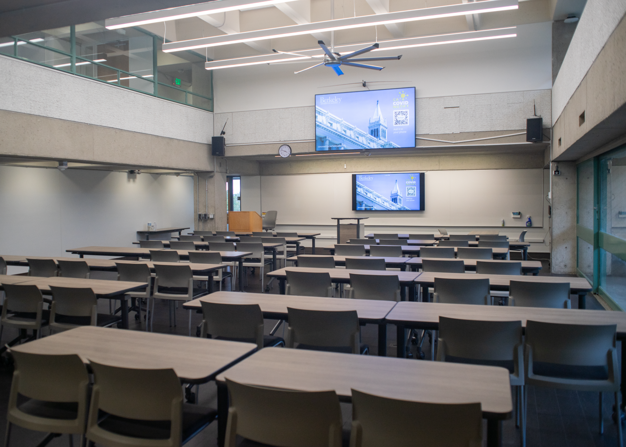 One of the classrooms at Mudd Hall with rows of desks in front of a podium and two large screens.
